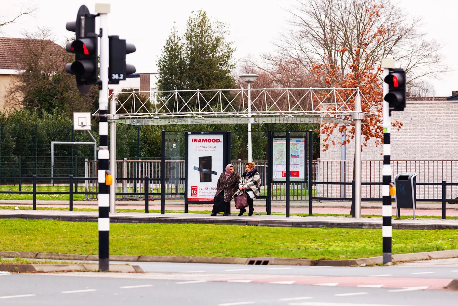 Twee mensen lopen langs een INAMOOD-abriposter bij een oversteekplaats