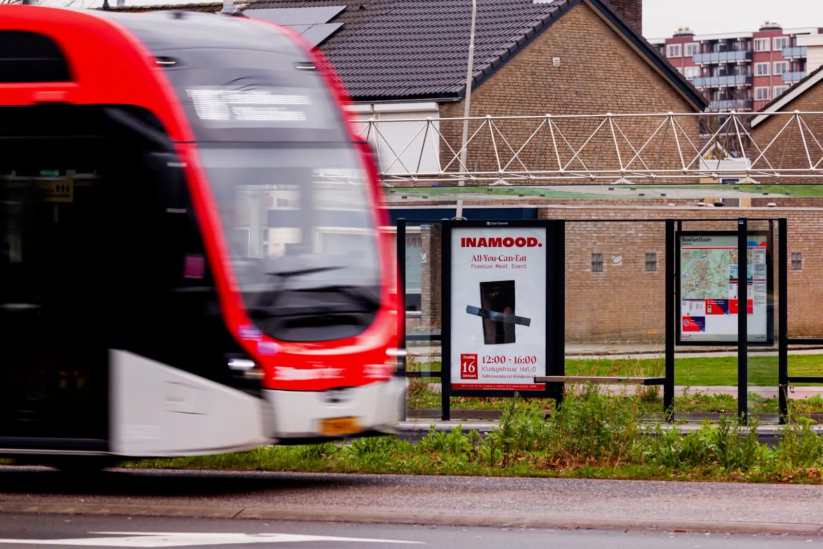 INAMOOD-abriposter bij een tramhalte terwijl een rode tram voorbijrijdt