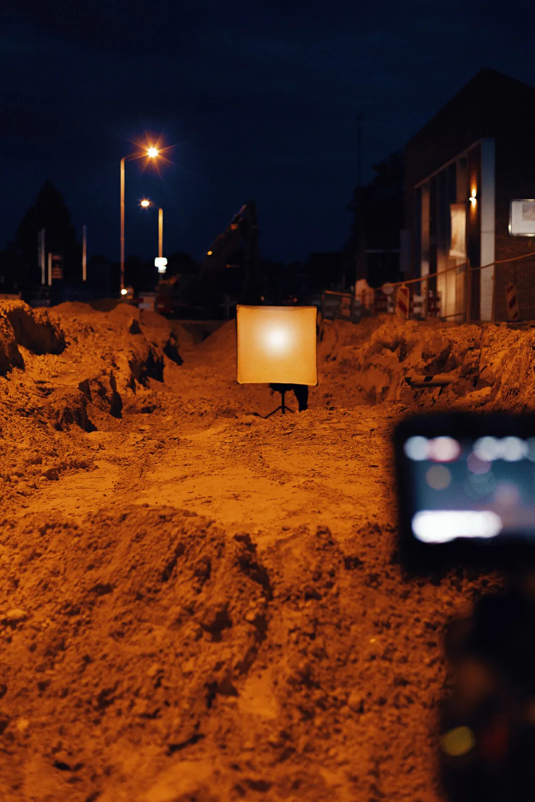 Het verlichte paneel in een opengebroken straat, donkere huizen erachter