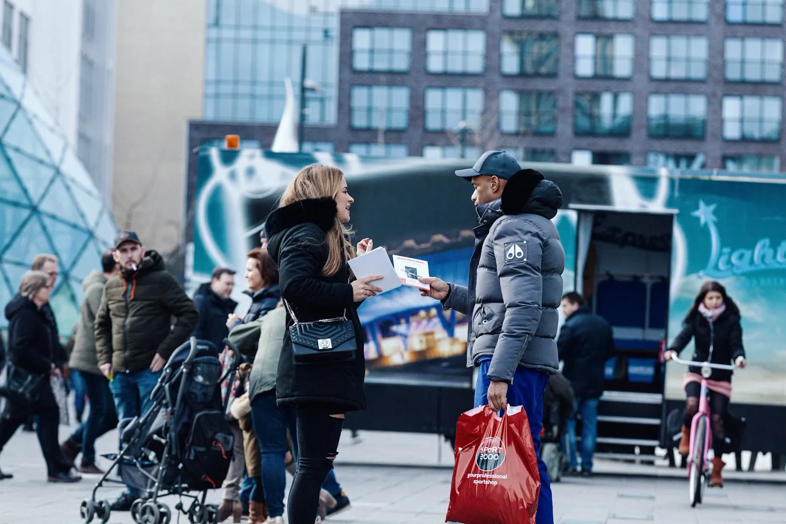 Een promotor geeft een INAMOOD-flyer aan een voorbijganger in het centrum