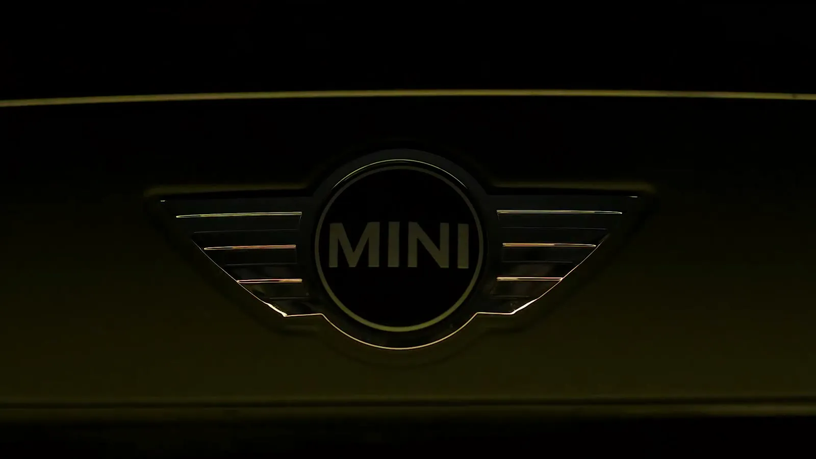 Het MINI-logo opgelicht in laag goudlicht op een zwarte motorkap