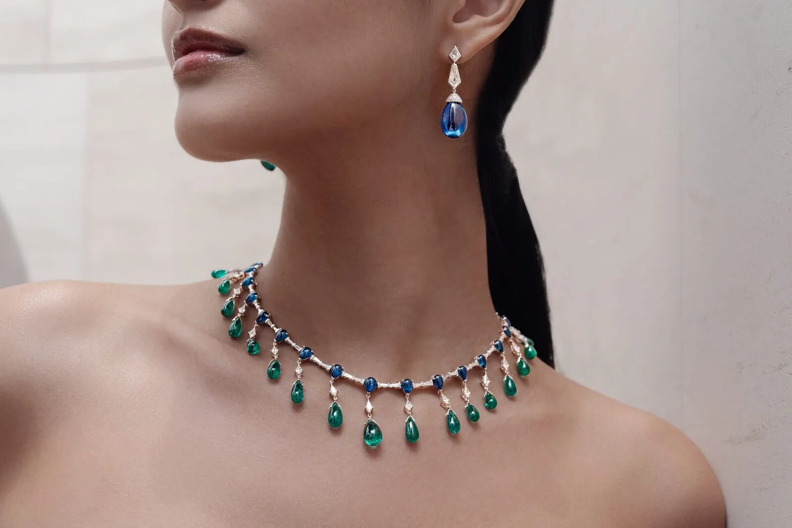 Collier met cabochon smaragd en saffier met bijpassende oorhanger, gedragen tegen lichte steen