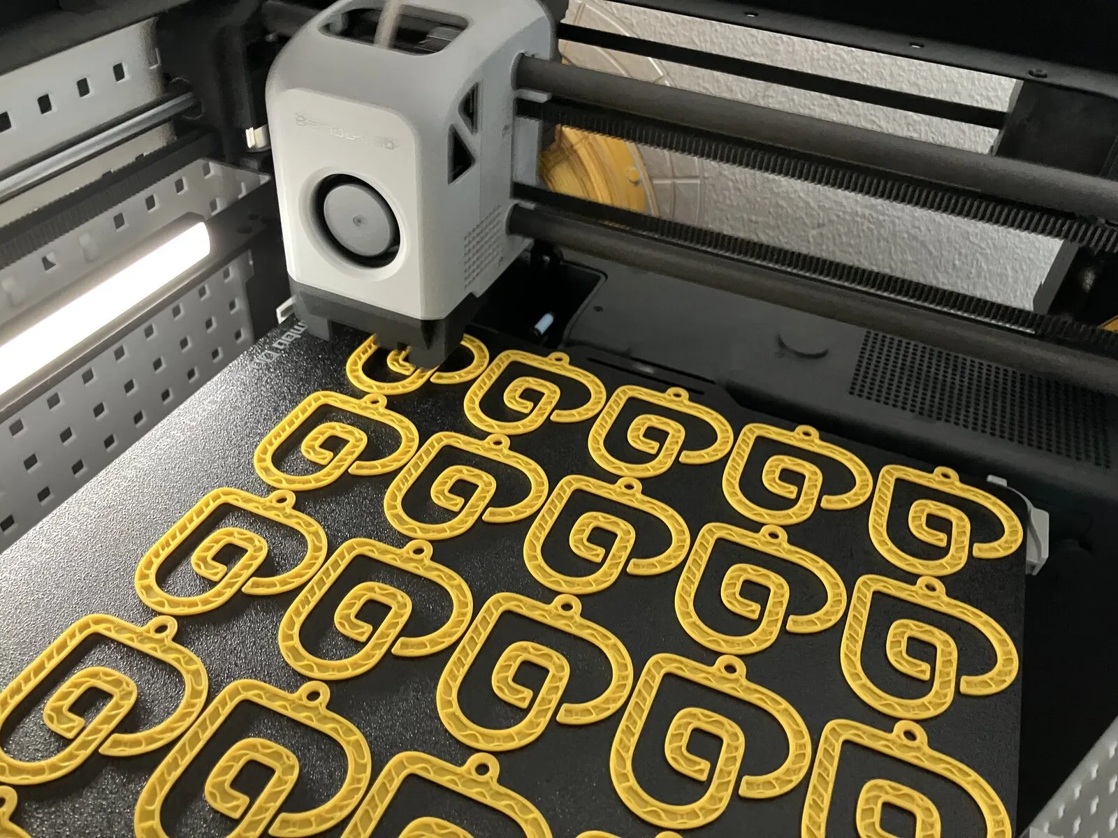 Rijen gele sleutelhangers op het printbed van de 3D-printer