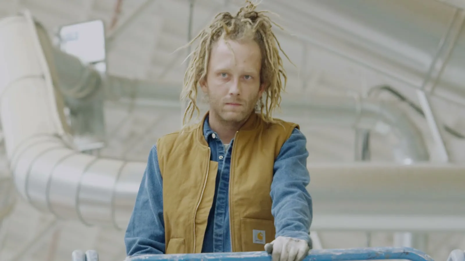 Een maker in een Carhartt-bodywarmer aan de machine, kijkend in de lens