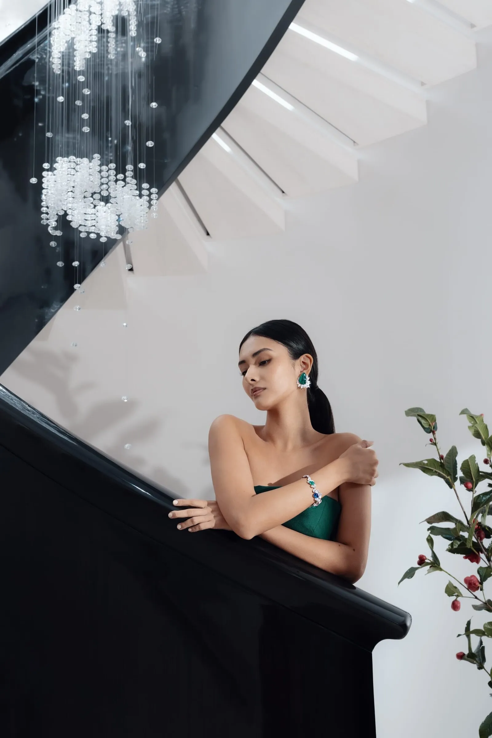 Model in een groene japon op de wenteltrap van de winkel onder de kristallen kroonluchter