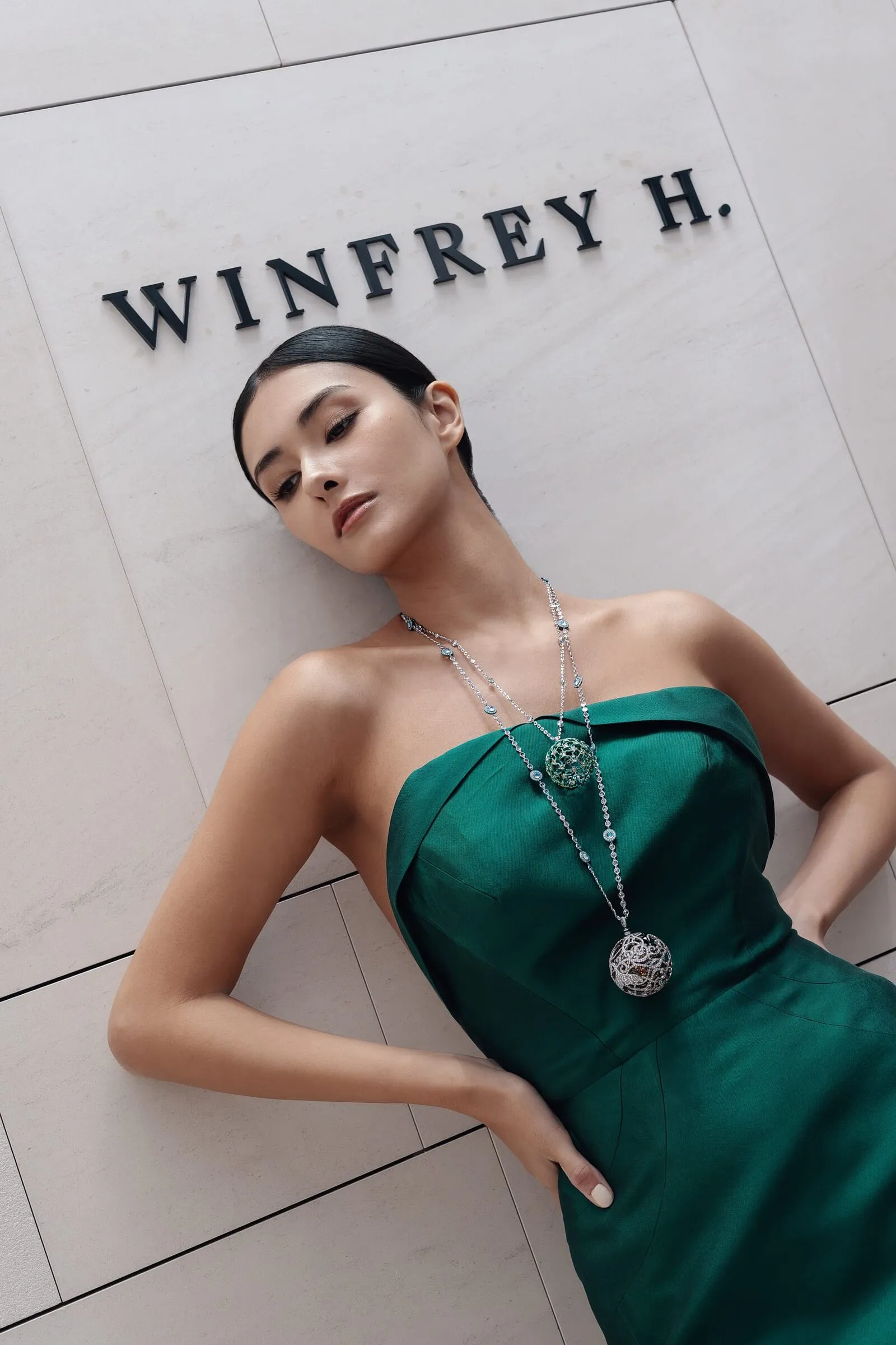 Model in een groene japon tegen de gevelwand, met de belettering van Winfrey H. erboven