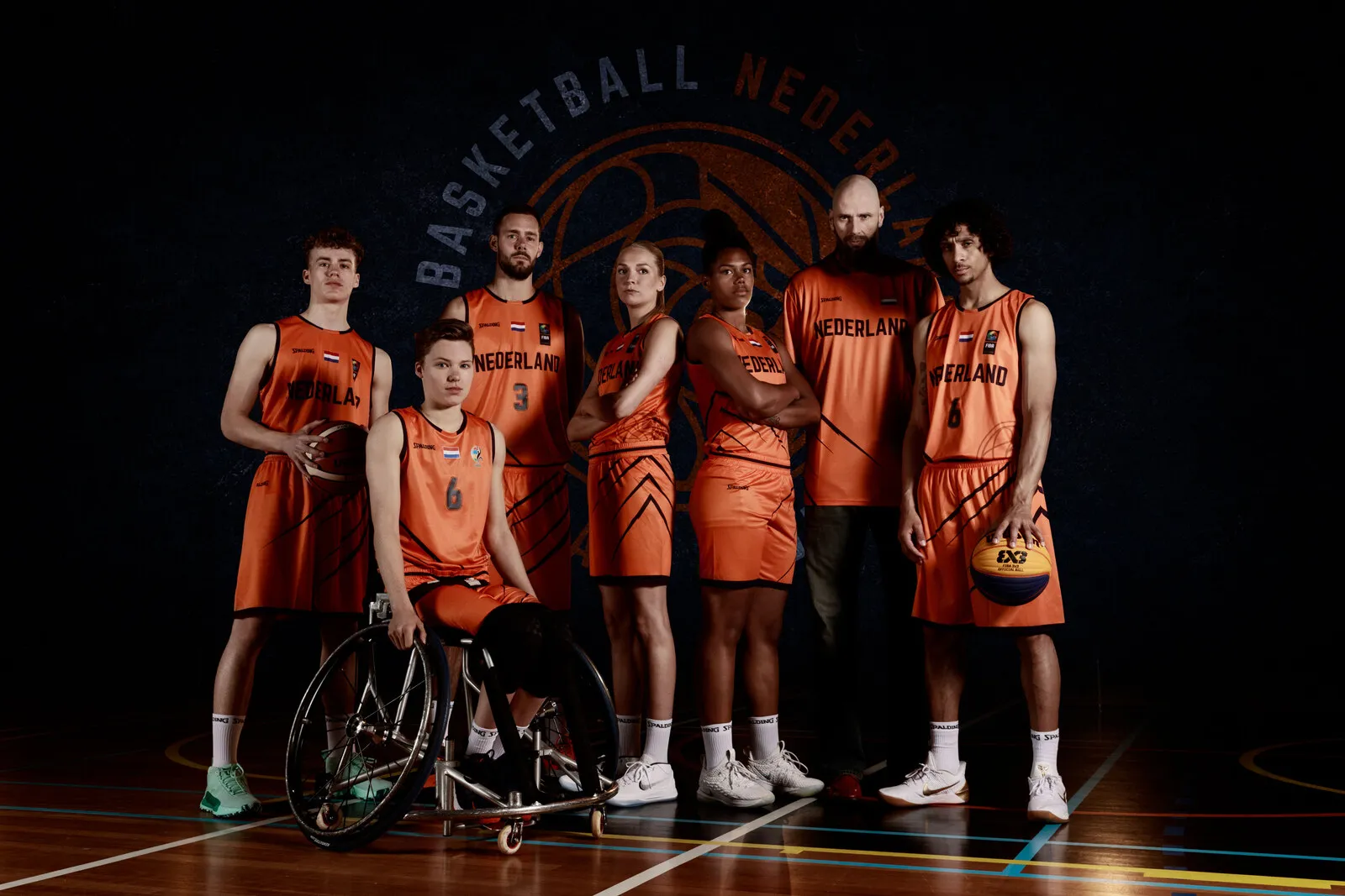 De Nederlandse selectie in oranje, uitgelicht voor het bondslogo op een donkere sportzaalachtergrond