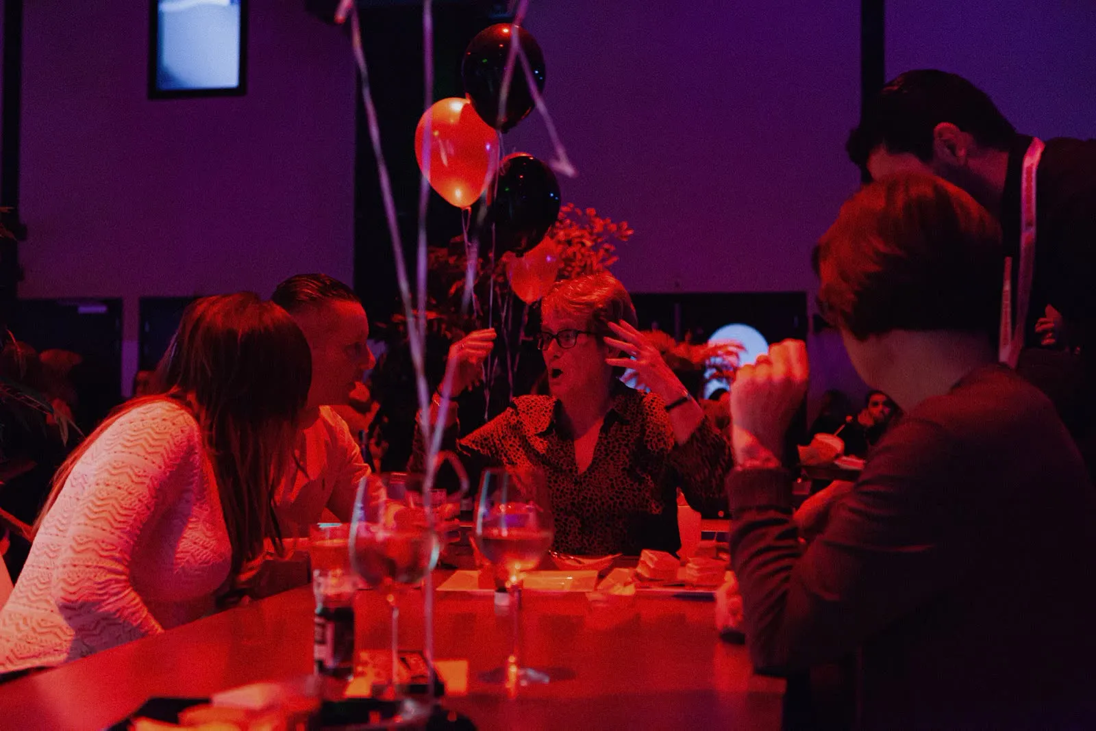 Gasten aan tafel onder rood licht met INAMOOD-ballonnen