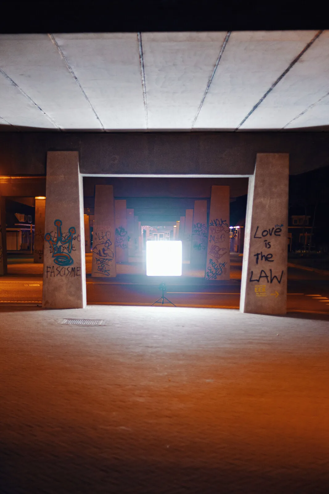 Een verlichte box alleen in een kaal betonnen onderdoorgang bij nacht, gefotografeerd voor Novaform