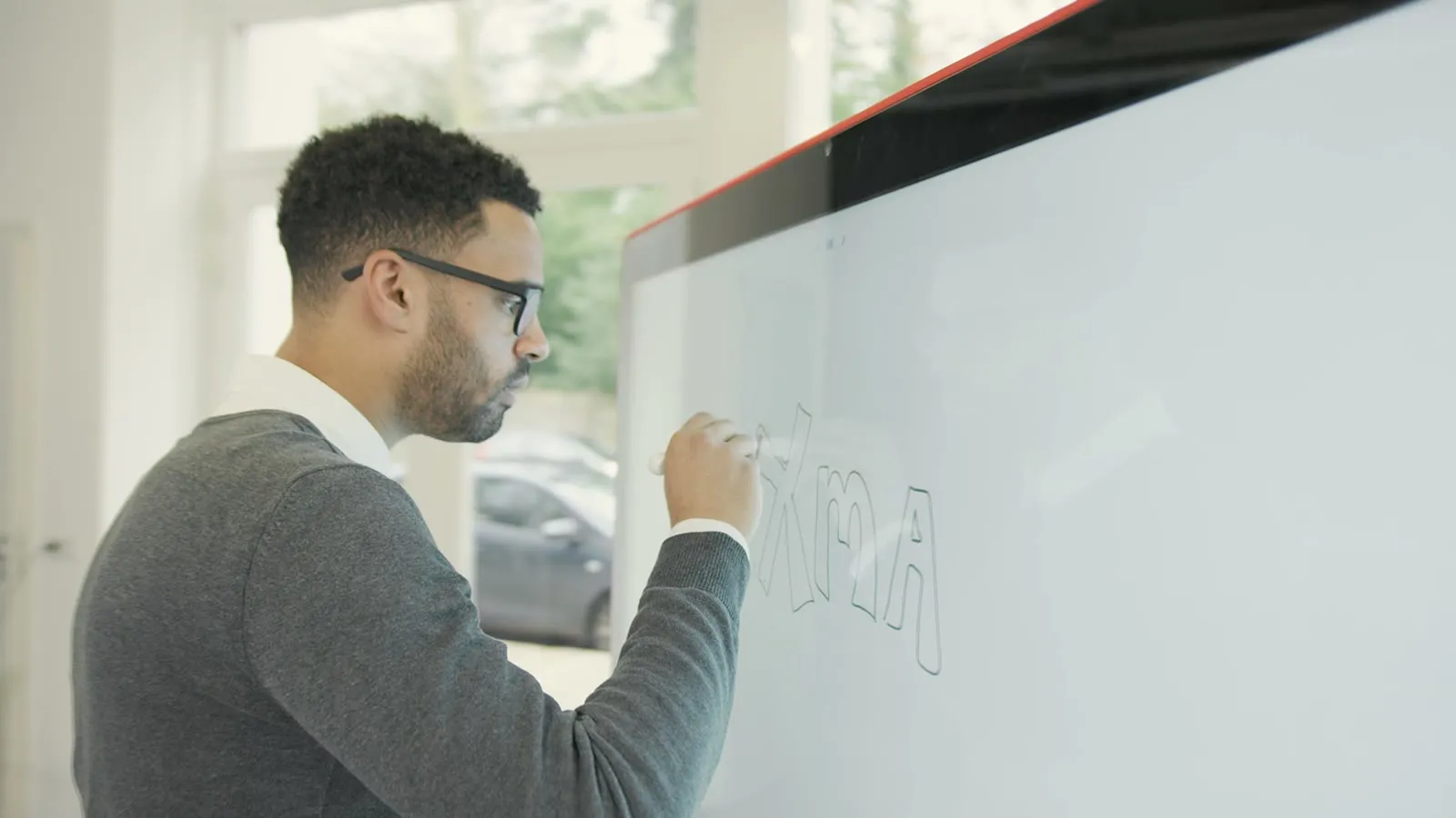 Een man tekent op de Jamboard, gezien door het glas van het scherm